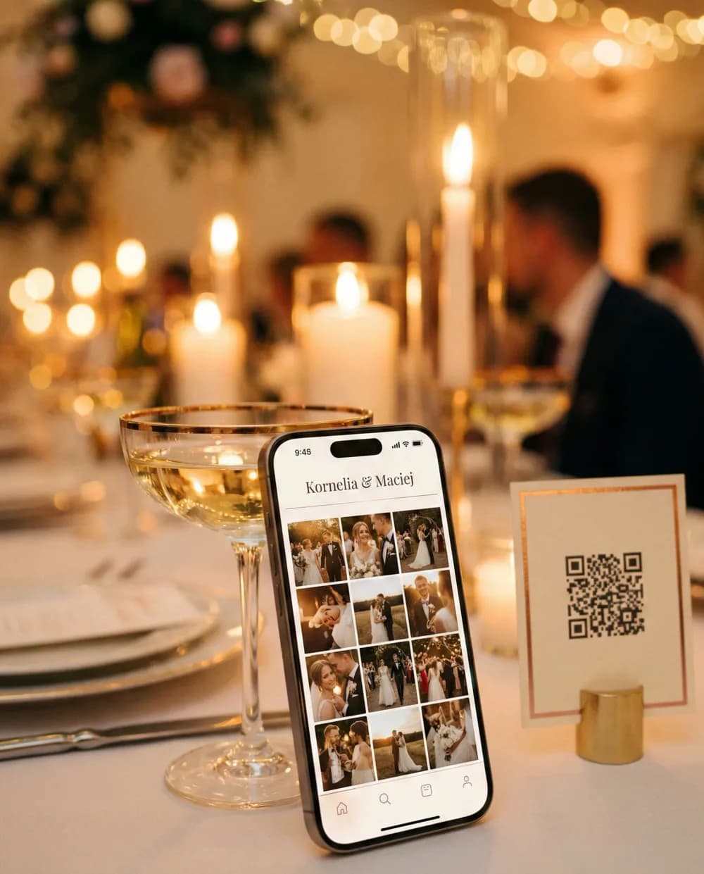 Telefon z galerią zdjęć pary oparty o kieliszek, obok stojak z kodem QR na weselnym stole